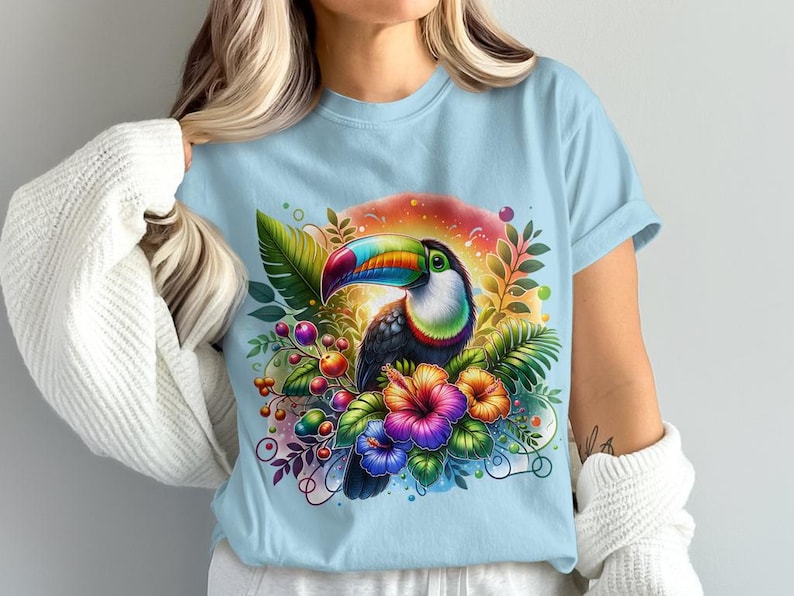 Pode incluir: Uma camiseta azul claro com uma estampa colorida de tucano e flores tropicais.