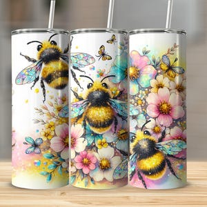 Pode incluir: Três copos de aço inoxidável com um design floral e de abelhas. Os copos apresentam uma ilustração em estilo aquarela de abelhas e flores em tons de rosa, azul e amarelo.