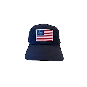 May include: A navy blue baseball cap with a white and red American flag patch featuring a blue clover design in the top left corner.