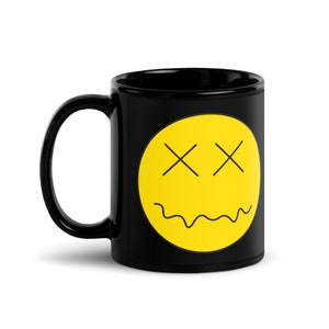 Può includere: Tazza in ceramica nera con un'emoticon gialla con occhi a croce e bocca ondulata. La tazza ha un manico nero e una finitura lucida. Ideale per caffè, tè o qualsiasi bevanda.