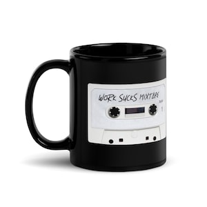 Könnte beinhalten: Schwarze Keramik-Tasse mit weißem Kassettenband-Design und dem Text "WORK SUCKS MIXTAPE". Die Tasse hat eine glänzende Oberfläche und einen gebogenen Griff. Ein lustiges Geschenk für Musikliebhaber.