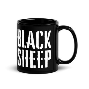 Può includere: Una tazza in ceramica nera con la scritta "BLACK SHEEP" in lettere bianche a stencil. La tazza ha un manico curvo e una finitura lucida, adatta per bevande calde.