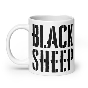 Può includere: Tazza in ceramica bianca con la scritta "BLACK SHEEP" in grassetto nero in stile stencil. La tazza ha un manico curvo e una finitura lucida, adatta per bevande calde o fredde.