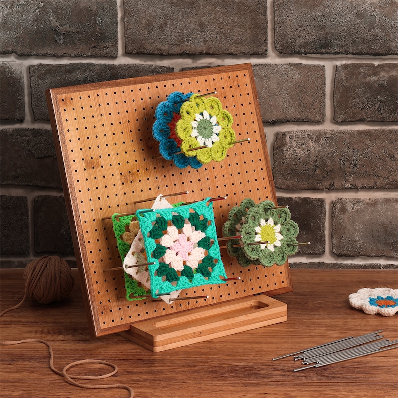 May include: A bamboo crochet project display stand with a pegboard and hooks to hold crocheted squares and flowers in green, blue, and yellow. The stand has a small shelf at the bottom.