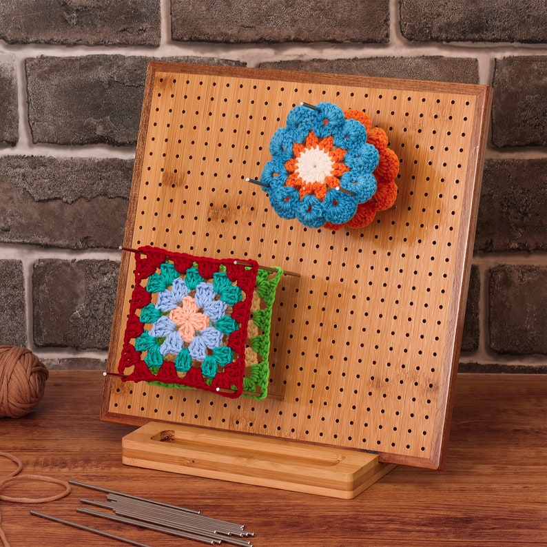 May include: A bamboo pegboard with a stand, used for displaying crocheted items. The pegboard has a variety of crocheted squares and flowers in red, green, blue, orange, and white.