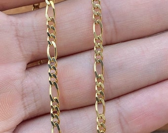 May include: Two gold chains, one on top of the other, are shown on a hand. The chains are both the same length and have a classic, flat, oval-shaped link design.