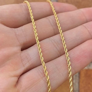 Op de afbeelding: Een gouden touwketting. De ketting is gemaakt van een gedraaid touwontwerp. De ketting ligt op de hand van een persoon.