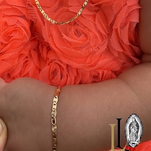 Puede incluir: Un conjunto de collar y pulsera de color dorado. El collar y la pulsera tienen un dise&ntilde;o delicado de eslabones planos con detalles de estrellas. Las joyas se exhiben sobre un fondo de tela naranja brillante y con volantes.