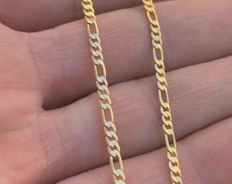 May include: A gold chain necklace with a figaro link pattern. The chain is shown on a hand.
