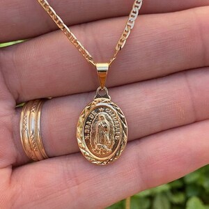 Op de afbeelding: Een gouden ketting met een gouden ovale hanger met een afbeelding van de Maagd Maria. De hanger heeft de woorden "Nuestra Señora de Guadalupe" gegraveerd rond de rand.