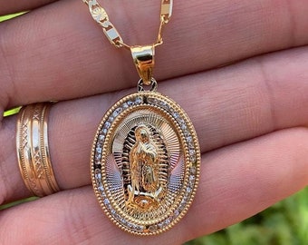 Op de afbeelding: Een gouden ketting met een hanger met een afbeelding van de Maagd Maria, omringd door kleine heldere stenen. De hanger is ovaalvormig en heeft een gedetailleerd ontwerp.