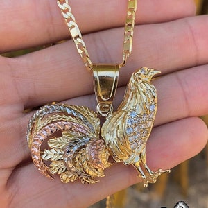 May include: A gold chain necklace with a three-toned rooster pendant. The rooster is detailed with a textured design and has clear rhinestones on its body.