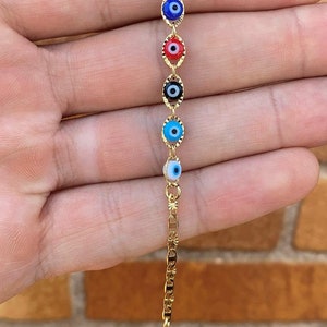 May include: Gold chain bracelet with five evil eye charms. The charms are blue, red, black, light blue, and white.