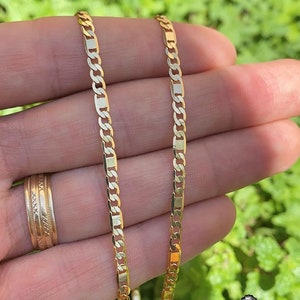 May include: Two gold chains with a curb link pattern. The chains are laid out side by side on a hand.