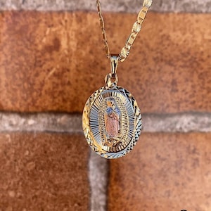 May include: A gold chain necklace with a two-tone oval pendant featuring an image of the Virgin Mary. The pendant has a diamond-shaped pattern.