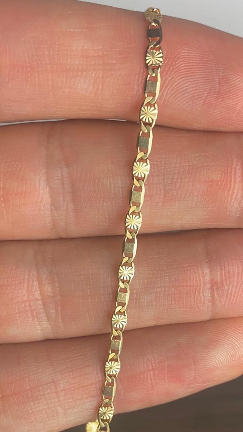 May include: A gold chain necklace with a delicate, patterned design. The chain is made of small, linked pieces that are intricately detailed.