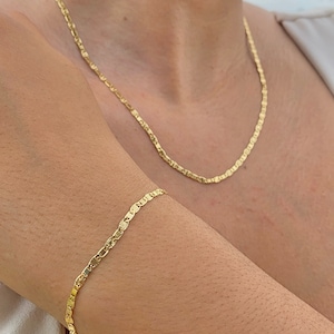 May include: A gold chain necklace and bracelet with a delicate, textured design. The necklace is worn around the neck and the bracelet is worn on the wrist.