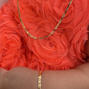 Puede incluir: Un conjunto de collar y pulsera de color dorado. El collar y la pulsera tienen un dise&ntilde;o delicado y enlazado con detalles de estrellas. Las joyas se exhiben sobre un fondo de tela naranja brillante y texturizada.