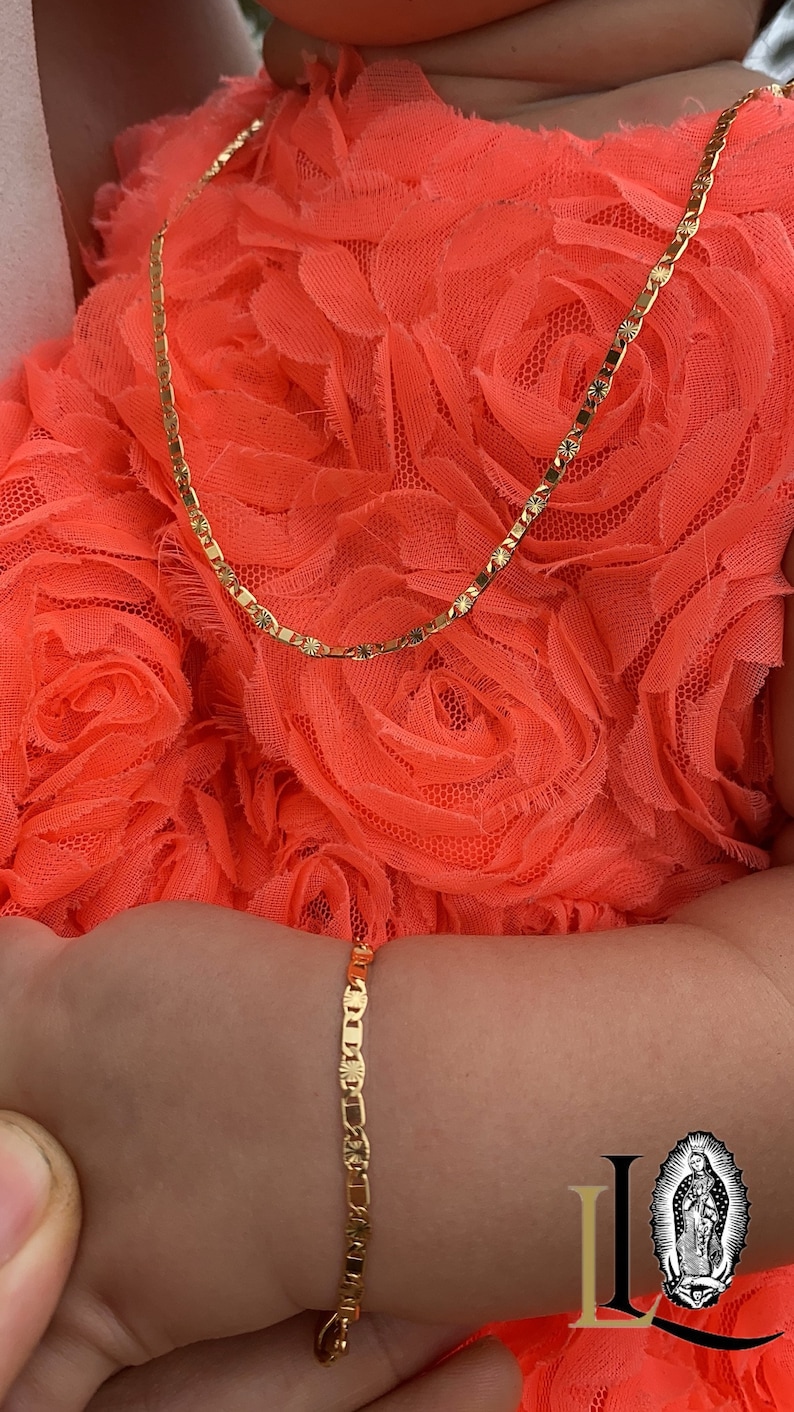 Puede incluir: Un conjunto de collar y pulsera de color dorado. El collar y la pulsera tienen un dise&ntilde;o delicado y enlazado con detalles de estrellas. Las joyas se exhiben sobre un fondo de tela naranja brillante y texturizada.