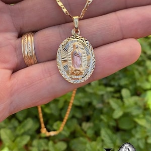 May include: A gold chain necklace with a two-tone oval pendant featuring a depiction of the Virgin Mary. The pendant has a detailed, textured design.