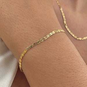 May include: A gold chain bracelet with a delicate, patterned design. The bracelet is worn on a person's wrist.