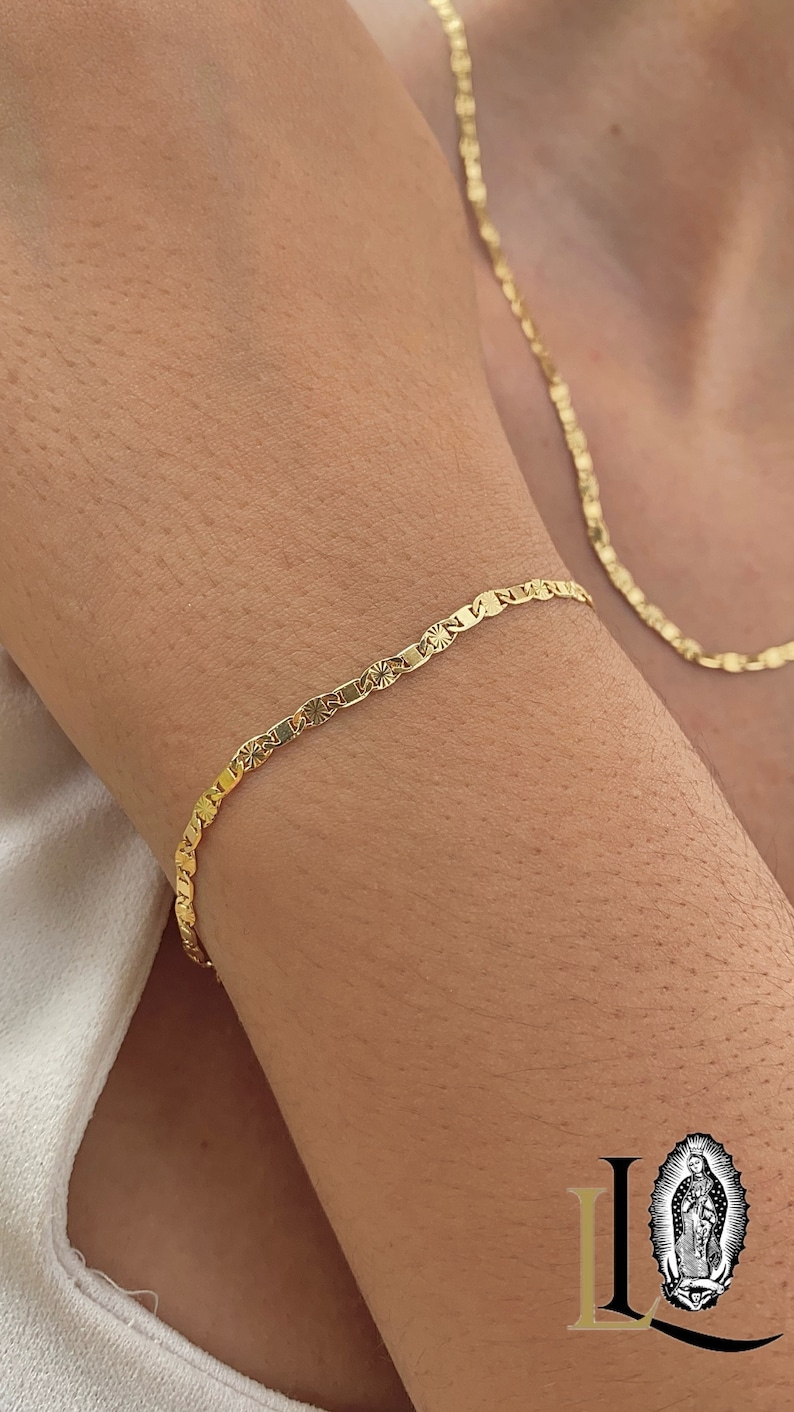 May include: A gold chain bracelet with a delicate, patterned design. The bracelet is worn on a person's wrist.