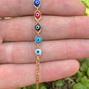 May include: A gold chain bracelet with five evil eye charms. The charms are blue, red, black, blue, and light blue with white pupils.