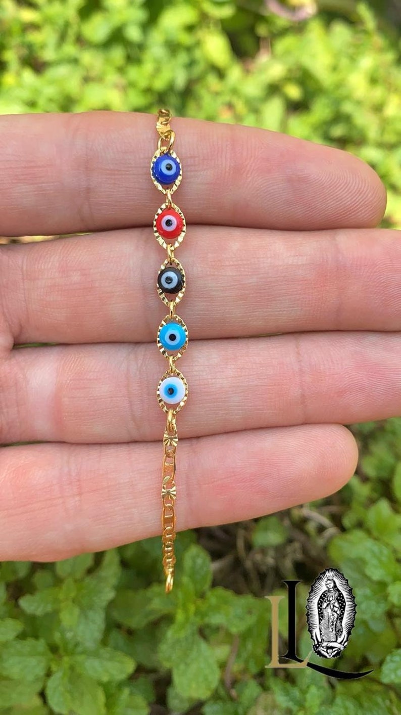 May include: A gold chain bracelet with five evil eye charms. The charms are blue, red, black, blue, and light blue with white pupils.