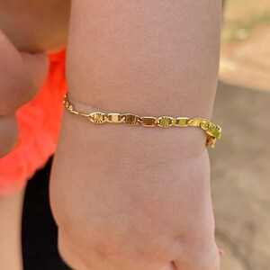 May include: A gold chain bracelet with a delicate design. The bracelet is on a child's wrist.