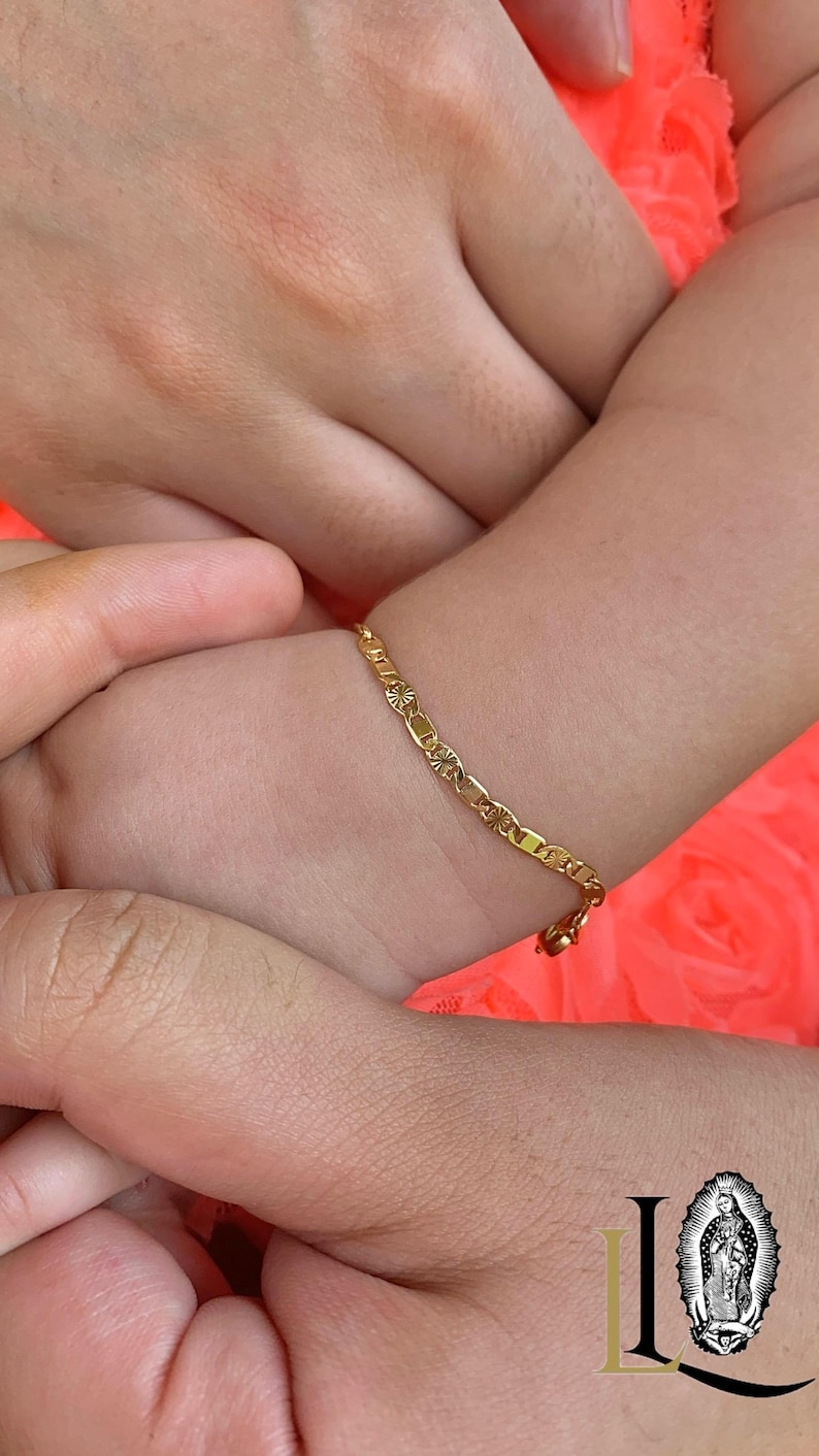 May include: A gold chain bracelet with a delicate design. The bracelet is worn on a child's wrist.