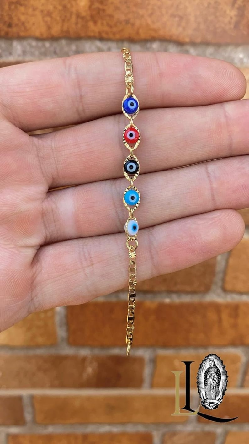 May include: A gold chain bracelet with five evil eye charms. The charms are blue, red, black, light blue, and white.