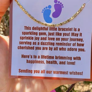 May include: A gold chain bracelet with a delicate design. The bracelet is displayed on a card with a message that reads: "This delightful little bracelet is a sparkling gem, just like you! May it sprinkle joy and love on your journey, serving as a dazzling reminder of how cherished you are by all who adore you. Here's to a lifetime brimming with happiness, health, and love! Sending you all our warmest wishes!"