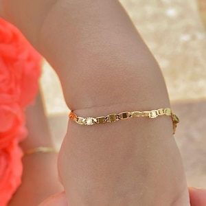 May include: A gold chain bracelet with a delicate, patterned design. The bracelet is worn on a child's wrist.