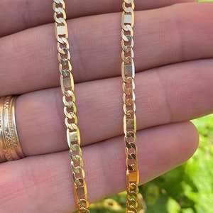 May include: A gold chain necklace with a curb link design. The chain is shown on a hand, with the links visible.