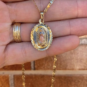 May include: A gold chain necklace with a pendant featuring a detailed image of the Virgin Mary. The pendant is oval-shaped and has a textured, diamond-cut design.