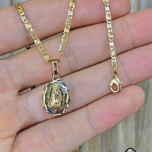 May include: A gold chain necklace with a pendant featuring a depiction of the Virgin Mary. The chain is a delicate, box-style chain with a small, ornate clasp.
