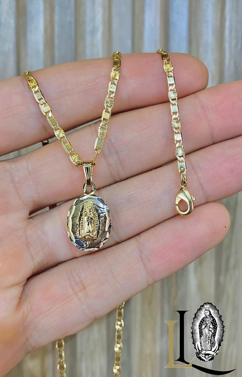 May include: A gold chain necklace with a pendant featuring a depiction of the Virgin Mary. The chain is a delicate, box-style chain with a small, ornate clasp.
