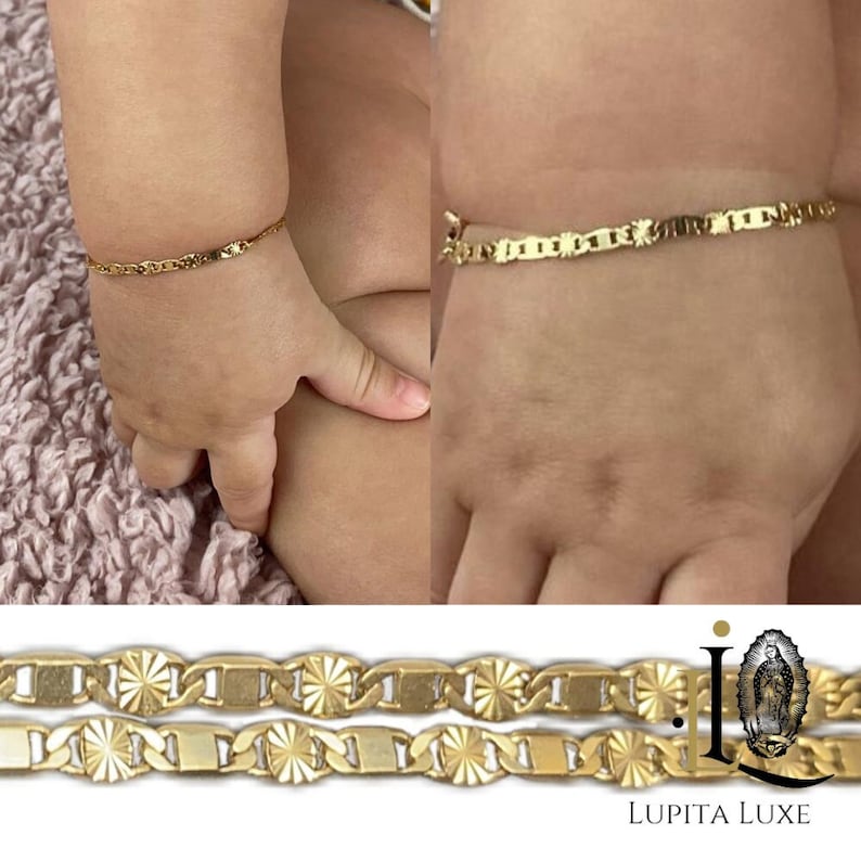 May include: Two gold bracelets with a detailed, patterned design. The bracelets are shown on a baby's wrist.