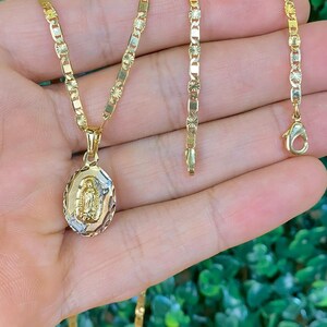 May include: A gold chain necklace with a pendant featuring a depiction of the Virgin Mary. The chain is a delicate, patterned design.