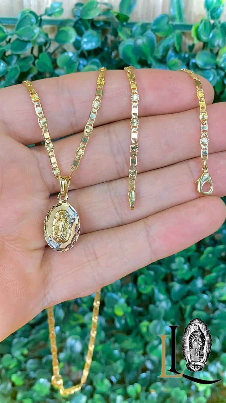 May include: A gold chain necklace with a pendant featuring a depiction of the Virgin Mary. The chain is a delicate, patterned design.