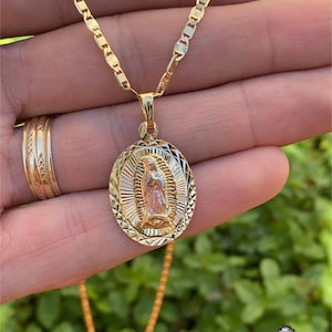 May include: A gold chain necklace with a detailed oval pendant featuring a depiction of the Virgin Mary. The pendant is two-toned, with a gold outer frame and a rose gold interior.