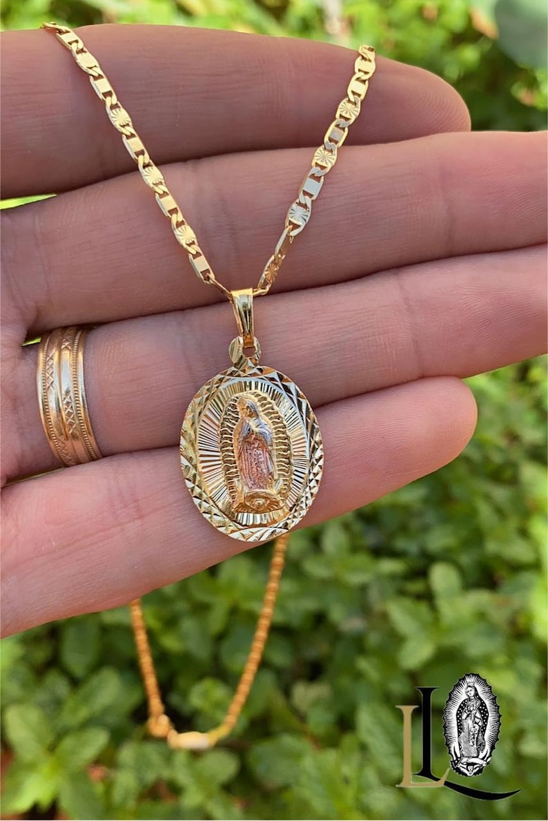 May include: A gold chain necklace with a detailed oval pendant featuring a depiction of the Virgin Mary. The pendant is two-toned, with a gold outer frame and a rose gold interior.