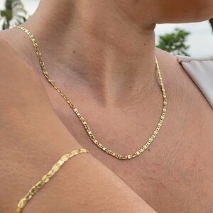 May include: A gold chain necklace and bracelet. The necklace is a delicate, thin chain with a slightly rounded link. The bracelet is a similar chain, but slightly thicker. Both pieces are made of gold metal.