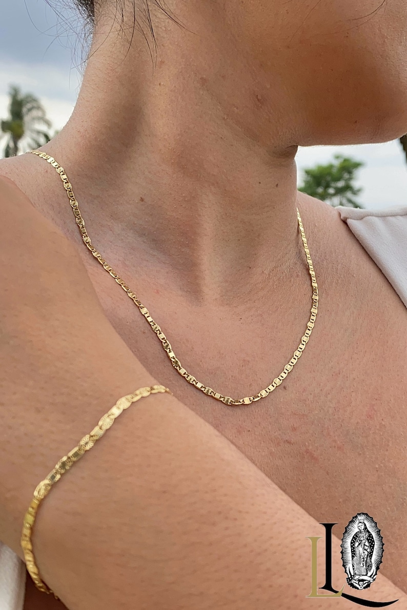 May include: A gold chain necklace and bracelet. The necklace is a delicate, thin chain with a slightly rounded link. The bracelet is a similar chain, but slightly thicker. Both pieces are made of gold metal.