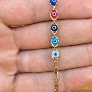 May include: Gold chain bracelet with five evil eye charms in different colors, including blue, red, black, and white.