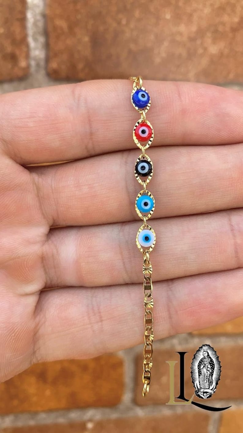 May include: Gold chain bracelet with five evil eye charms in different colors, including blue, red, black, and white.
