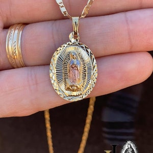 May include: A gold chain necklace with a round pendant featuring a detailed image of the Virgin Mary. The pendant is two-toned, with a gold and rose gold finish.