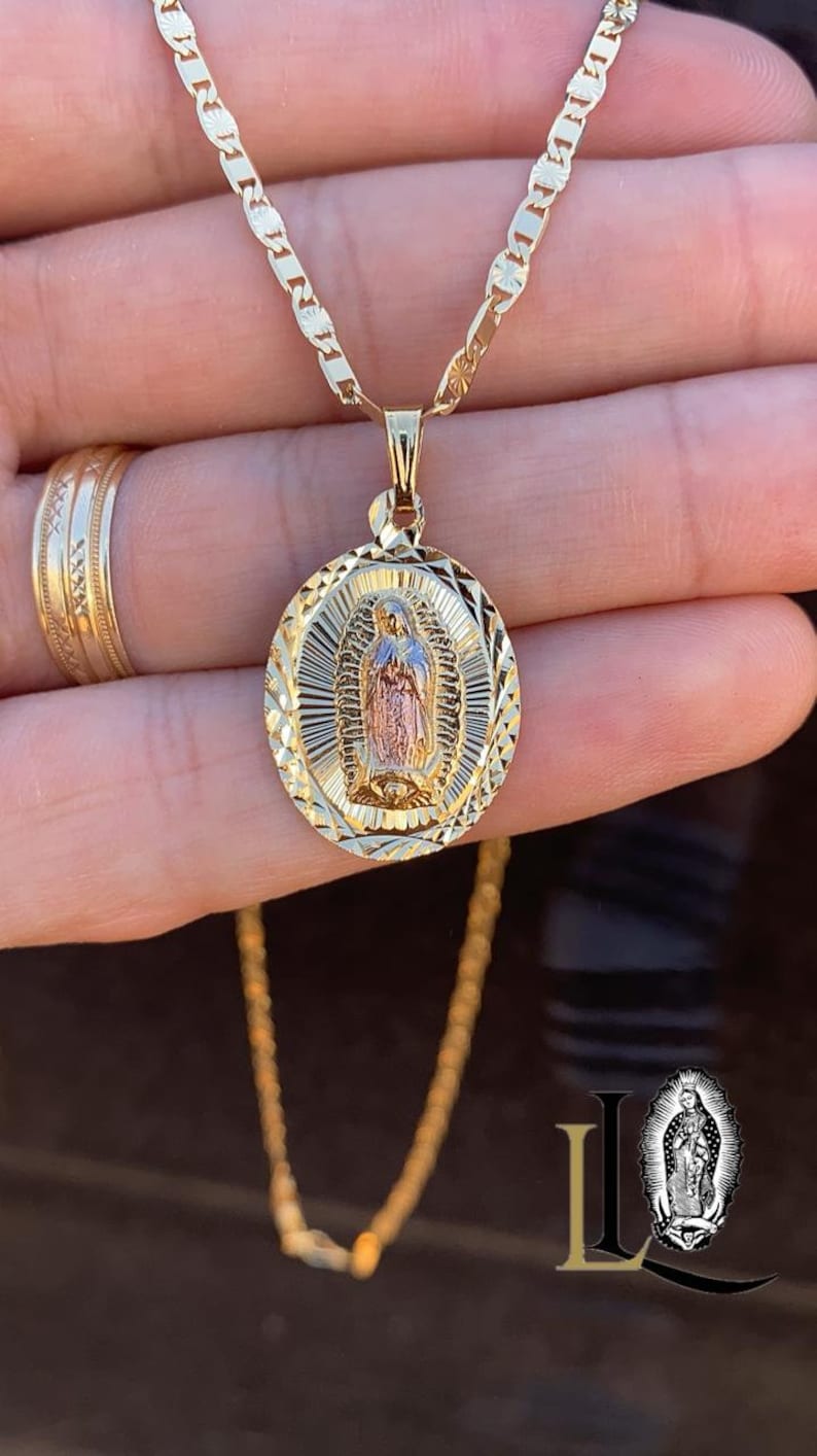 May include: A gold chain necklace with a round pendant featuring a detailed image of the Virgin Mary. The pendant is two-toned, with a gold and rose gold finish.