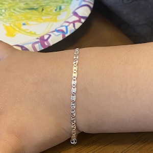 May include: A silver chain bracelet with a delicate, patterned design. The bracelet is on a person's wrist.