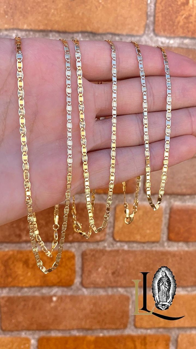 May include: Four gold chains with a diamond-shaped pattern on a hand. The chains are different lengths and are all made of gold.